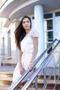 Beautiful brunette stands on the steps, a shopping center, pink dress Royalty Free Stock Photo