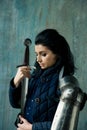 Beautiful brunette woman in ancient iron knightly armor. Medieval female knight in armor against the background of an ancient wall