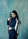 Beautiful brunette woman in ancient iron knightly armor. Medieval female knight in armor against the background of an ancient wall