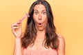 Beautiful brunette woman asking for depilation holding shaver razor over yellow background scared and amazed with open mouth for