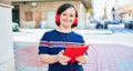 Beautiful brunette woman with down syndrome at the town on a sunny day using touchpad device listening to music wearing headphones Royalty Free Stock Photo