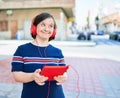 Beautiful brunette woman with down syndrome at the town on a sunny day using touchpad device listening to music wearing headphones Royalty Free Stock Photo