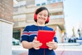 Beautiful brunette woman with down syndrome at the town on a sunny day using touchpad device listening to music wearing headphones Royalty Free Stock Photo