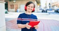 Beautiful brunette woman with down syndrome at the town on a sunny day using touchpad device listening to music wearing headphones Royalty Free Stock Photo