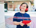 Beautiful brunette woman with down syndrome at the town on a sunny day using touchpad device listening to music wearing headphones Royalty Free Stock Photo