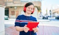 Beautiful brunette woman with down syndrome at the town on a sunny day using touchpad device listening to music wearing headphones Royalty Free Stock Photo