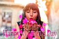 Beautiful brunette woman with flowers blowing petals from her hands. Happy International Women`s Day text with blurred background Royalty Free Stock Photo