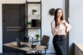 Beautiful brunette woman having a morning coffee, standing near at her desk in the office. Young woman drinking coffee at the Royalty Free Stock Photo