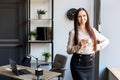 Beautiful brunette woman having a morning coffee, standing near at her desk in the office. Young woman drinking coffee at the Royalty Free Stock Photo