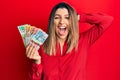Beautiful brunette woman holding australian dollars crazy and scared with hands on head, afraid and surprised of shock with open