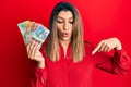 Beautiful brunette woman holding australian dollars pointing down with fingers showing advertisement, surprised face and open