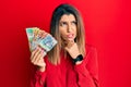 Beautiful brunette woman holding australian dollars thinking worried about a question, concerned and nervous with hand on chin