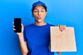 Beautiful brunette woman holding delivery paper bag and showing smartphone screen looking at the camera blowing a kiss being Royalty Free Stock Photo