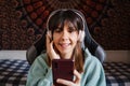 A beautiful brunette woman listening to an audio with her headphones at home. She is holding her phone while sitting on a chair in