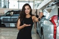 Beautiful brunette woman manager smiling holding car keys in her hand standing in dealership center near brand new SUV Royalty Free Stock Photo