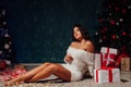 Beautiful brunette woman opens presents at Christmas tree with garland lights Royalty Free Stock Photo