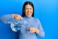 Beautiful brunette woman pouring water in glass sticking tongue out happy with funny expression Royalty Free Stock Photo