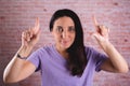 Beautiful brunette woman raising two index fingers on a brick wall background Royalty Free Stock Photo