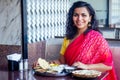 Beautiful brunette woman in red sari eating with appetite traditional thali wirh rise,curd,dal in Goa restaurant masala Royalty Free Stock Photo