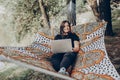 Beautiful brunette woman relaxing on hammock outdoors near lake in the forest, freelancer working in the park while resting in Royalty Free Stock Photo