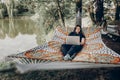 Beautiful brunette woman relaxing on hammock outdoors near lake in the forest, freelancer working in the park while resting in Royalty Free Stock Photo