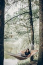Beautiful brunette woman relaxing on hammock outdoors near lake in the forest, freelancer working in the park while resting in Royalty Free Stock Photo