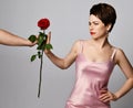 Beautiful brunette woman with short hair in pink silk dress and earrings standing and refusing to get red rose from mans hand Royalty Free Stock Photo