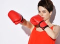 Beautiful brunette woman with short hair in red sport top, earrings and red boxing gloves pushing with hands Royalty Free Stock Photo