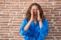 Beautiful brunette woman standing over bricks wall shouting angry out loud with hands over mouth Royalty Free Stock Photo