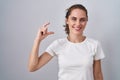 Beautiful brunette woman standing over isolated background smiling and confident gesturing with hand doing small size sign with Royalty Free Stock Photo