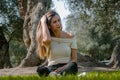 Beautiful brunette woman touching her long hair. She sits in a park on green grass. Royalty Free Stock Photo