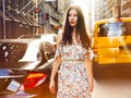 Beautiful brunette woman walking on New York city street between cars wearing summer dress at sunny summer day. Royalty Free Stock Photo