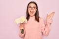 Beautiful brunette woman wearing glasses holding bouquet of flowers over pink background celebrating victory with happy smile and Royalty Free Stock Photo