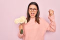 Beautiful brunette woman wearing glasses holding bouquet of flowers over pink background screaming proud, celebrating victory and Royalty Free Stock Photo