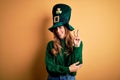 Beautiful brunette woman wearing green hat with clover celebrating saint patricks day smiling with happy face winking at the