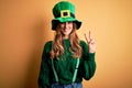 Beautiful brunette woman wearing green hat with clover celebrating saint patricks day smiling with happy face winking at the