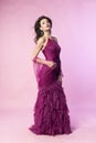 Beautiful brunette woman wearing a purple dress, with wind blown hair, posing standing on a pink background. Advertising and Royalty Free Stock Photo