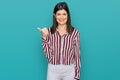 Beautiful brunette woman wearing striped shirt smiling with happy face looking and pointing to the side with thumb up Royalty Free Stock Photo