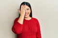 Beautiful brunette woman wearing wool winter sweater covering one eye with hand, confident smile on face and surprise emotion Royalty Free Stock Photo