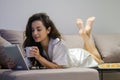 Beautiful brunette woman in white robe lying on bed in living room alone tapping on tablet holding cup of coffee Royalty Free Stock Photo