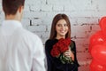 Beautiful brunette young woman in a blue dress with a large bouquet of red roses looking at his boyfriend on a brick wall Royalty Free Stock Photo