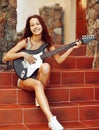 Beautiful brunette young woman with guitar sitting on stairs Royalty Free Stock Photo