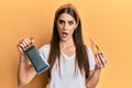 Beautiful brunette young woman holding grater and cheese in shock face, looking skeptical and sarcastic, surprised with open mouth Royalty Free Stock Photo