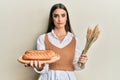 Beautiful brunette young woman holding homemade bread and spike wheat depressed and worry for distress, crying angry and afraid