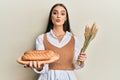 Beautiful brunette young woman holding homemade bread and spike wheat looking at the camera blowing a kiss being lovely and sexy