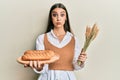 Beautiful brunette young woman holding homemade bread and spike wheat puffing cheeks with funny face