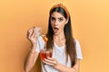 Beautiful brunette young woman holding honey in shock face, looking skeptical and sarcastic, surprised with open mouth Royalty Free Stock Photo