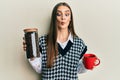 Beautiful brunette young woman holding jar with coffee beans and drinking coffee cup making fish face with mouth and squinting Royalty Free Stock Photo