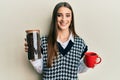 Beautiful brunette young woman holding jar with coffee beans and drinking coffee cup smiling with a happy and cool smile on face Royalty Free Stock Photo