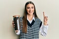 Beautiful brunette young woman holding jar with coffee beans smiling with an idea or question pointing finger with happy face, Royalty Free Stock Photo